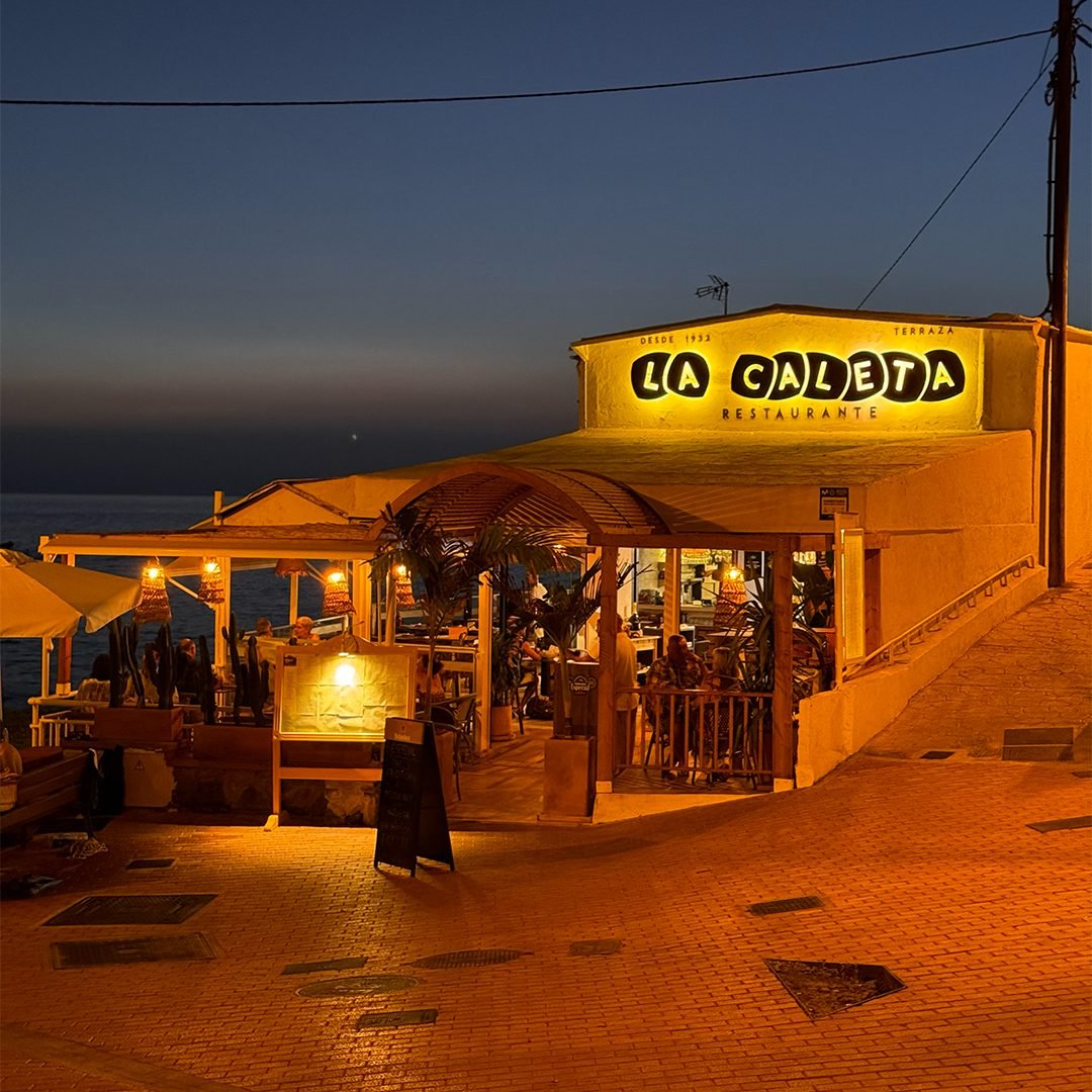 Fachada del Restaurante La Caleta iluminada al anochecer junto al mar, Adeje